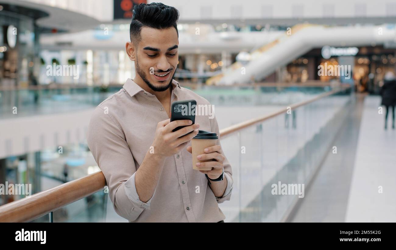 Uomo indiano Ispanico tipo imprenditore datore di lavoro uomo d'affari bere caffè tè navigazione scorrimento schermo del telefono cellulare acquisto online chat con Foto Stock