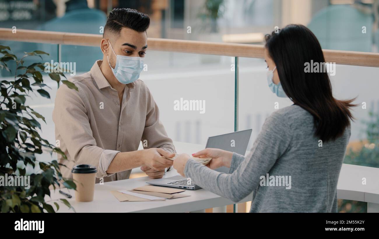 Indiano ispanico uomo banca lavoratore consulente agente di assicurazione in maschera medica consulta cliente ragazza dare prestito denaro denaro dollari pagamento bancario finanziario Foto Stock