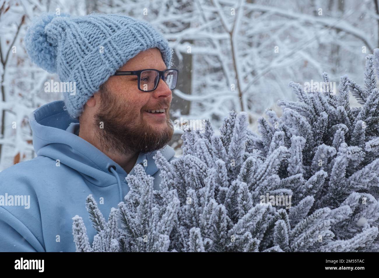 Un uomo sorridente guarda un albero di Natale innevato nelle sue mani Foto Stock