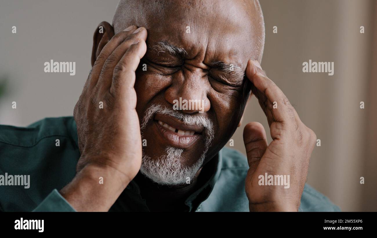 Primo piano viso triste anziano afro-americano sensazione di mal di testa emicrania cronica non sano nonno multirazziale massaggiare templi non sano di mezza età Foto Stock