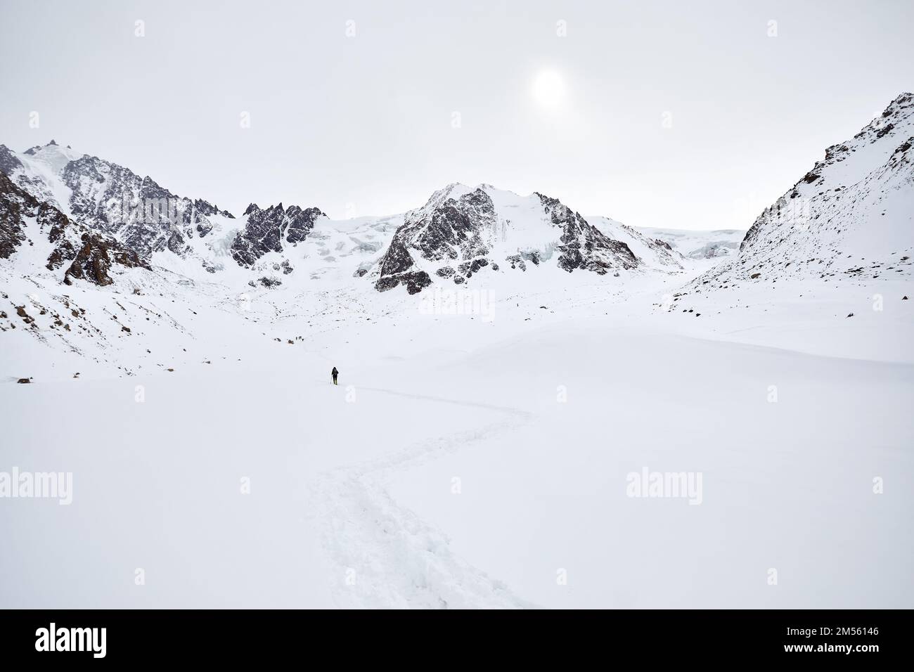 Uomo con zaino a piedi sulla collina di neve nelle belle montagne contro cielo nuvoloso in Almaty, Kazakistan Foto Stock