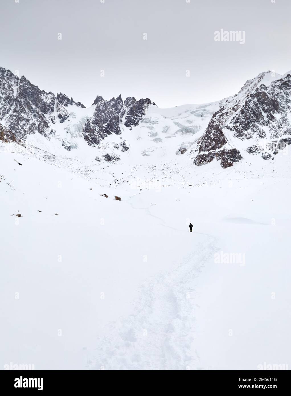 Piccolo uomo con zaino a piedi sulla collina di neve nelle belle montagne contro cielo nuvoloso in Almaty, Kazakistan Foto Stock