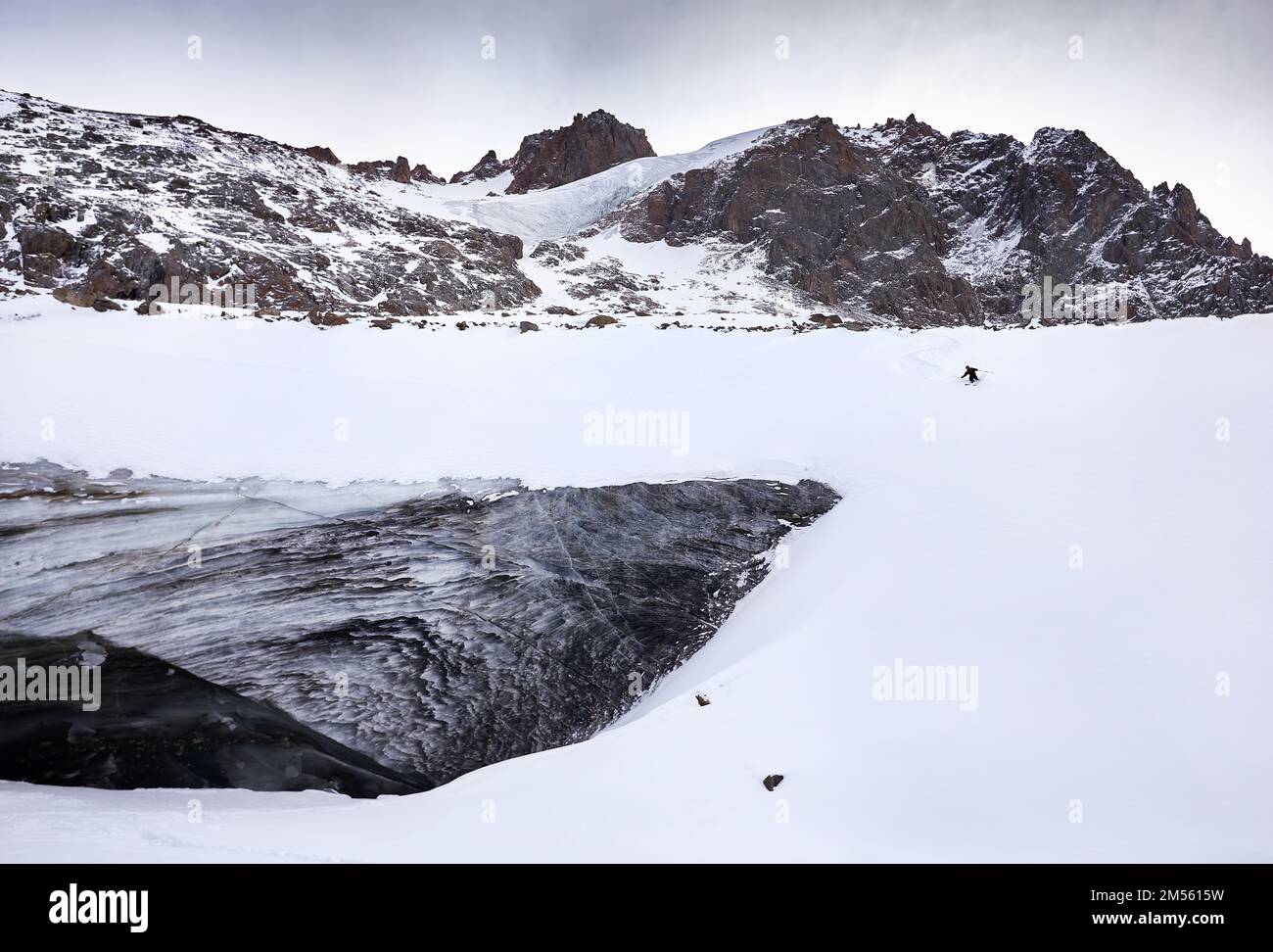 Sciatore uomo sciare in discesa con zaino rosso in casco e maschera in alte montagne innevate vicino al muro di ghiaccio con spruzzi di neve. Sport estremi all'aperto in wint Foto Stock
