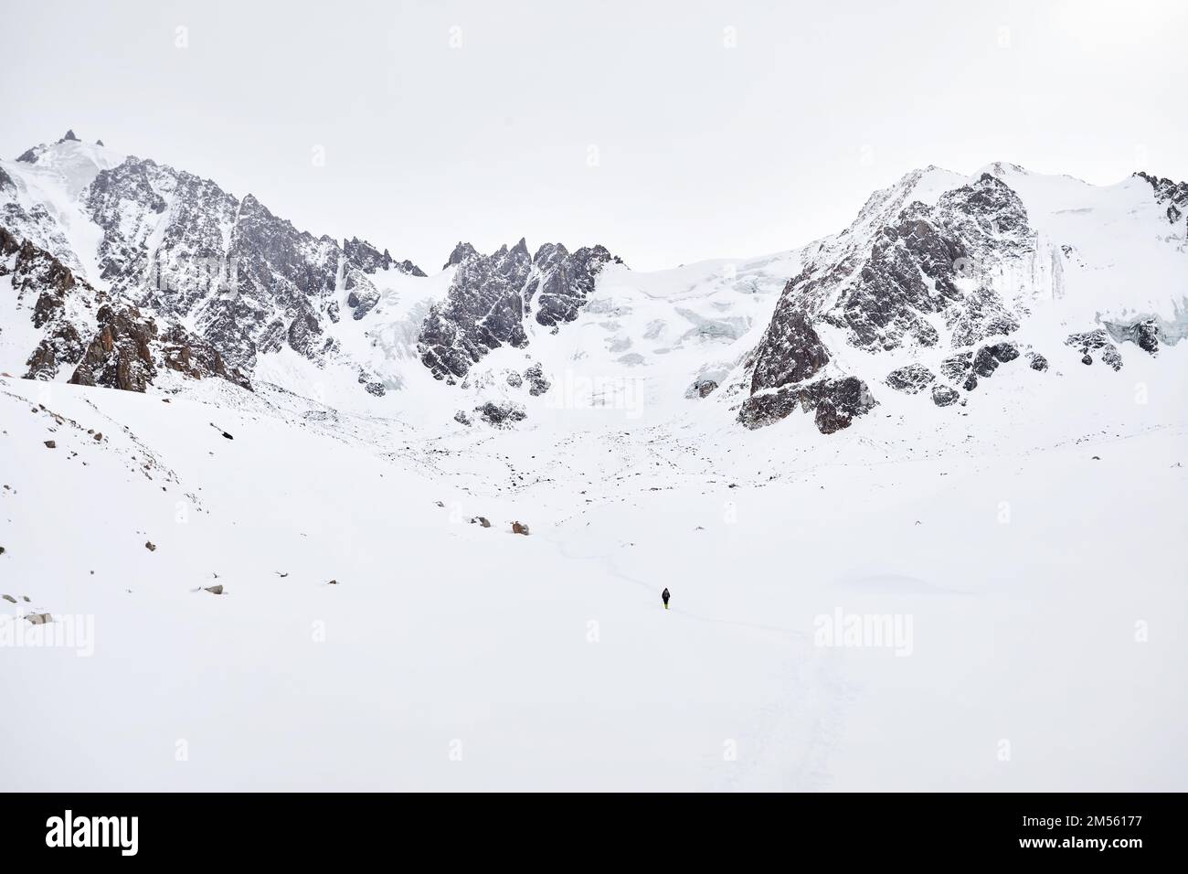 Piccolo uomo con zaino a piedi sulla collina di neve nelle belle montagne contro cielo nuvoloso in Almaty, Kazakistan Foto Stock