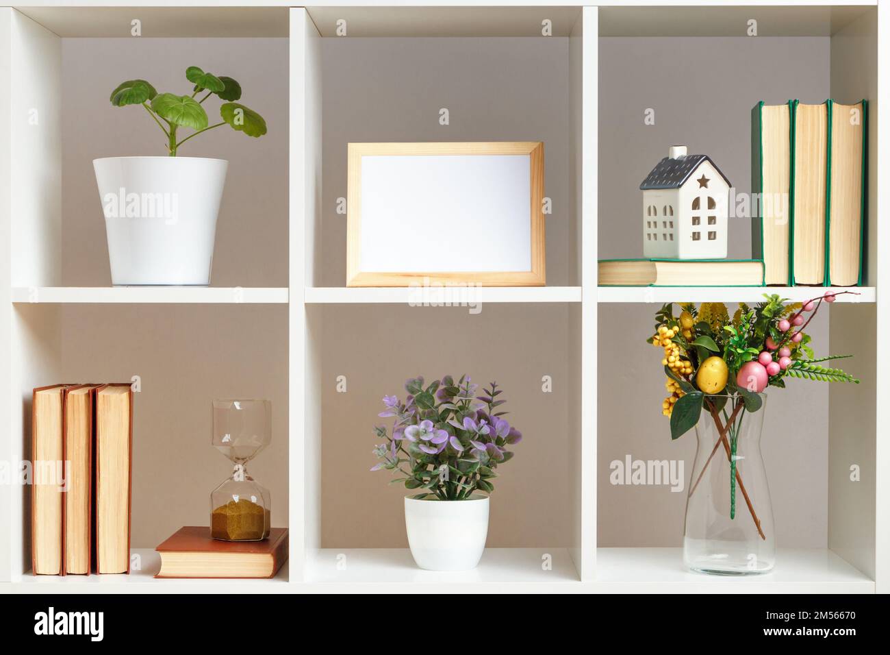 Interni per la casa, elementi decorativi pasquali. Mensole bianche con libri, clessidra e piante Foto Stock