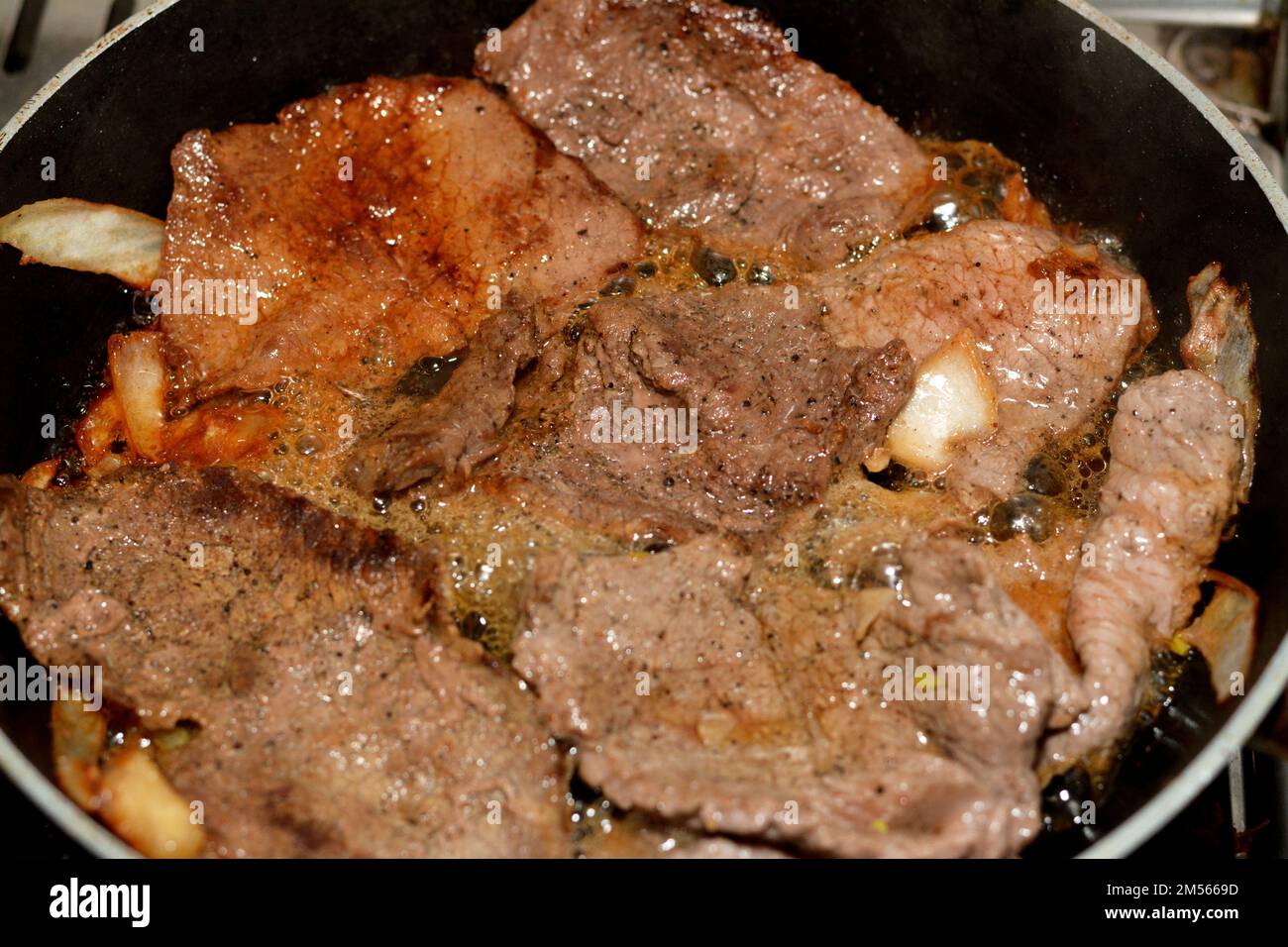 Pezzi di bistecca di carne alla griglia con olio, fette di cipolla, sale e  pepe nero in una padella alla griglia, bistecche di manzo selezionate in  fase di cottura, ricetta di carne