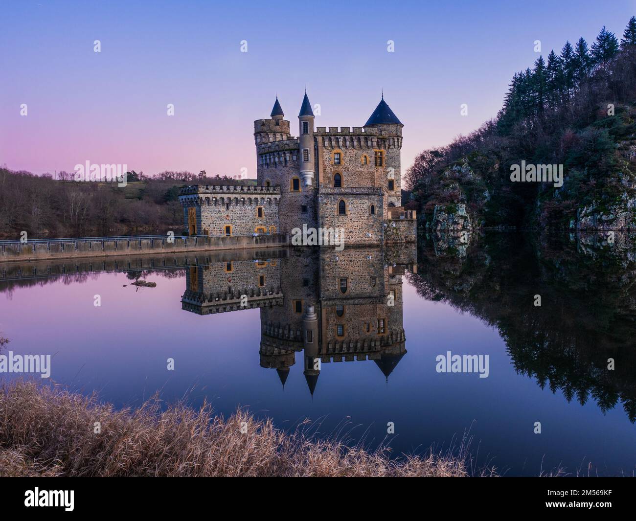 Il castello Chateau de la Roche Castello a Saint-Priest-la-Roche, Francia si riflette in acqua al tramonto Foto Stock