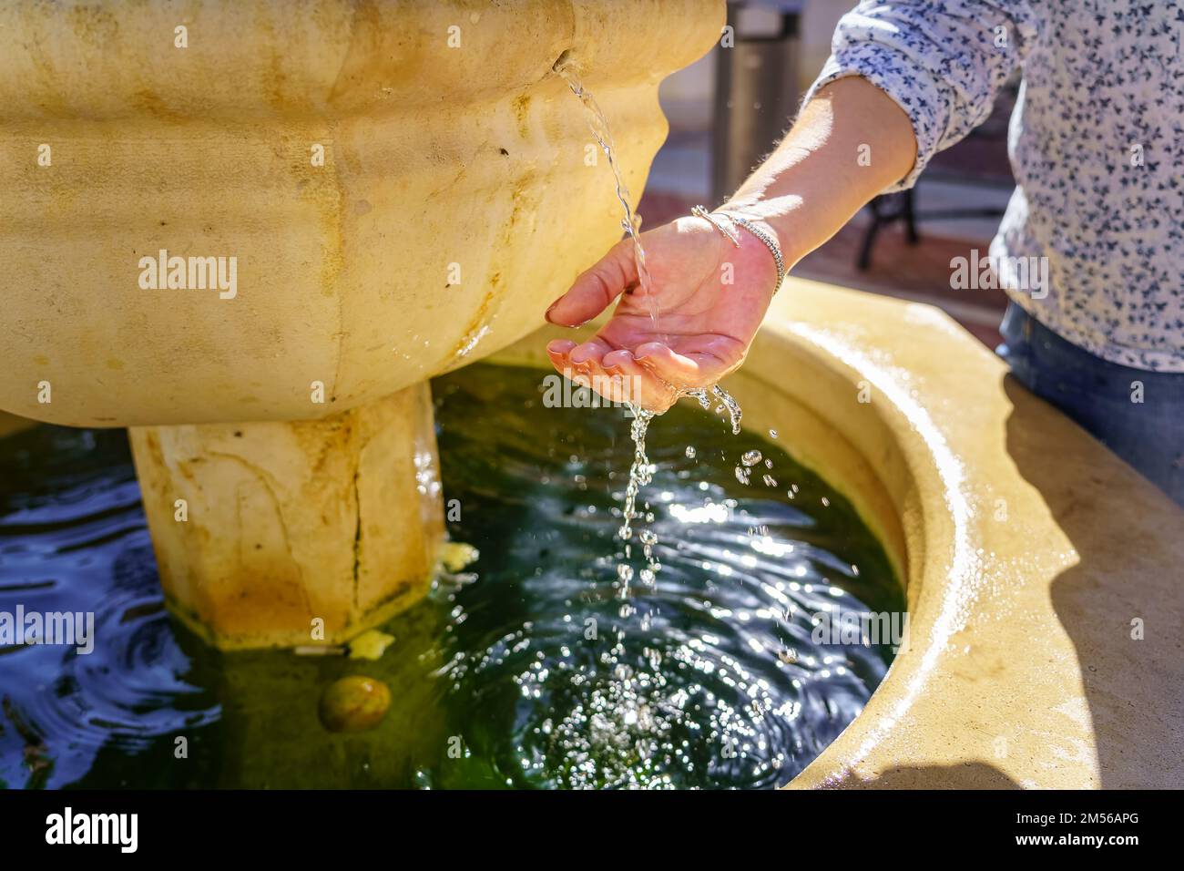 Mano di donna che tocca l'acqua dolce di una fontana di origine romanica nella città di Ecija, Siviglia. Foto Stock