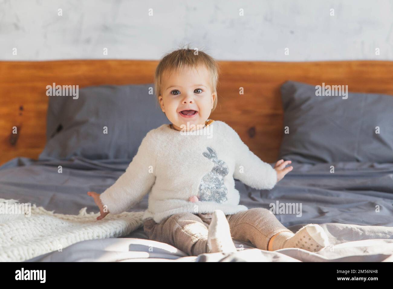 Il bambino cute si trova sul letto e ride in modo che due denti siano visibili Foto Stock