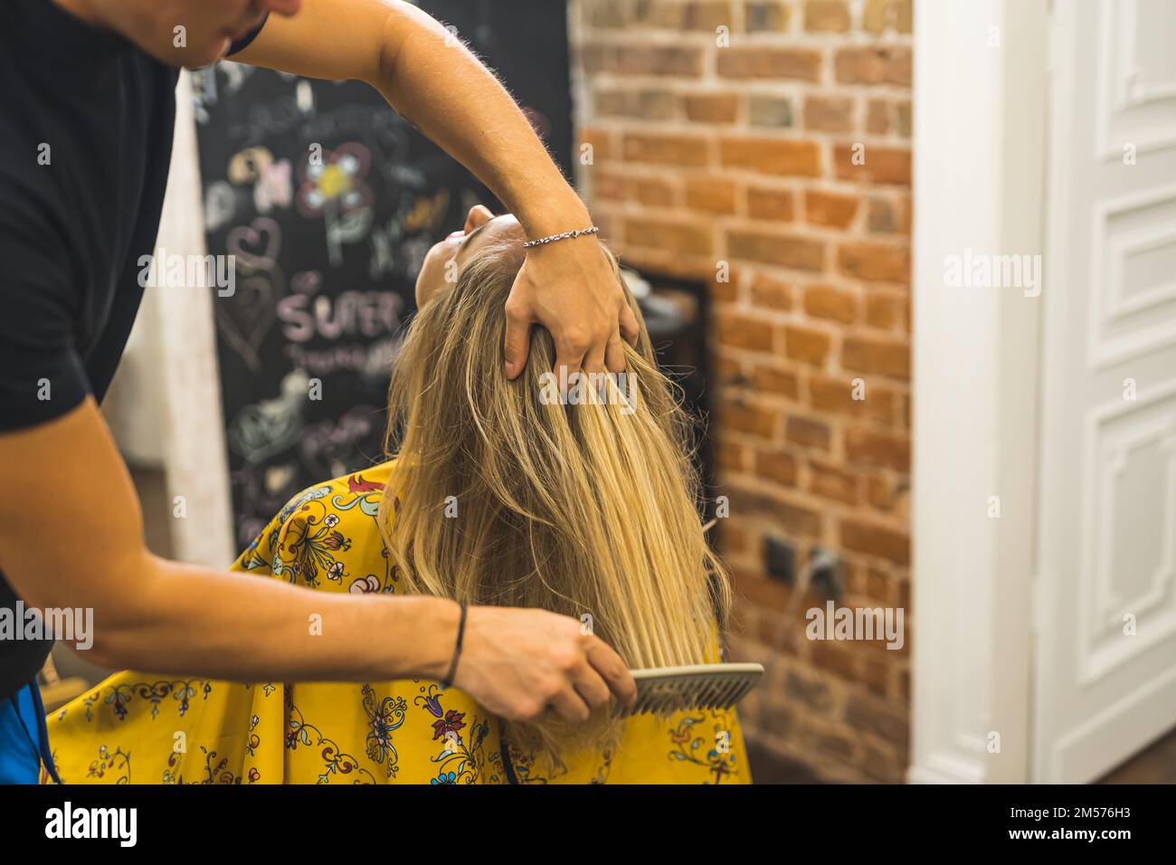 Pettinare i capelli. Parrucchiere professionista che usa un pettine sui capelli biondi del suo cliente. Concetto esperto di parrucchiere. Foto di alta qualità Foto Stock