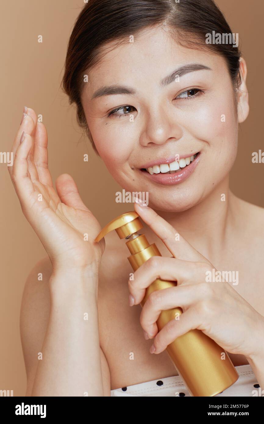 moderna donna asiatica con mousse auto abbronzante isolata su sfondo beige. Foto Stock