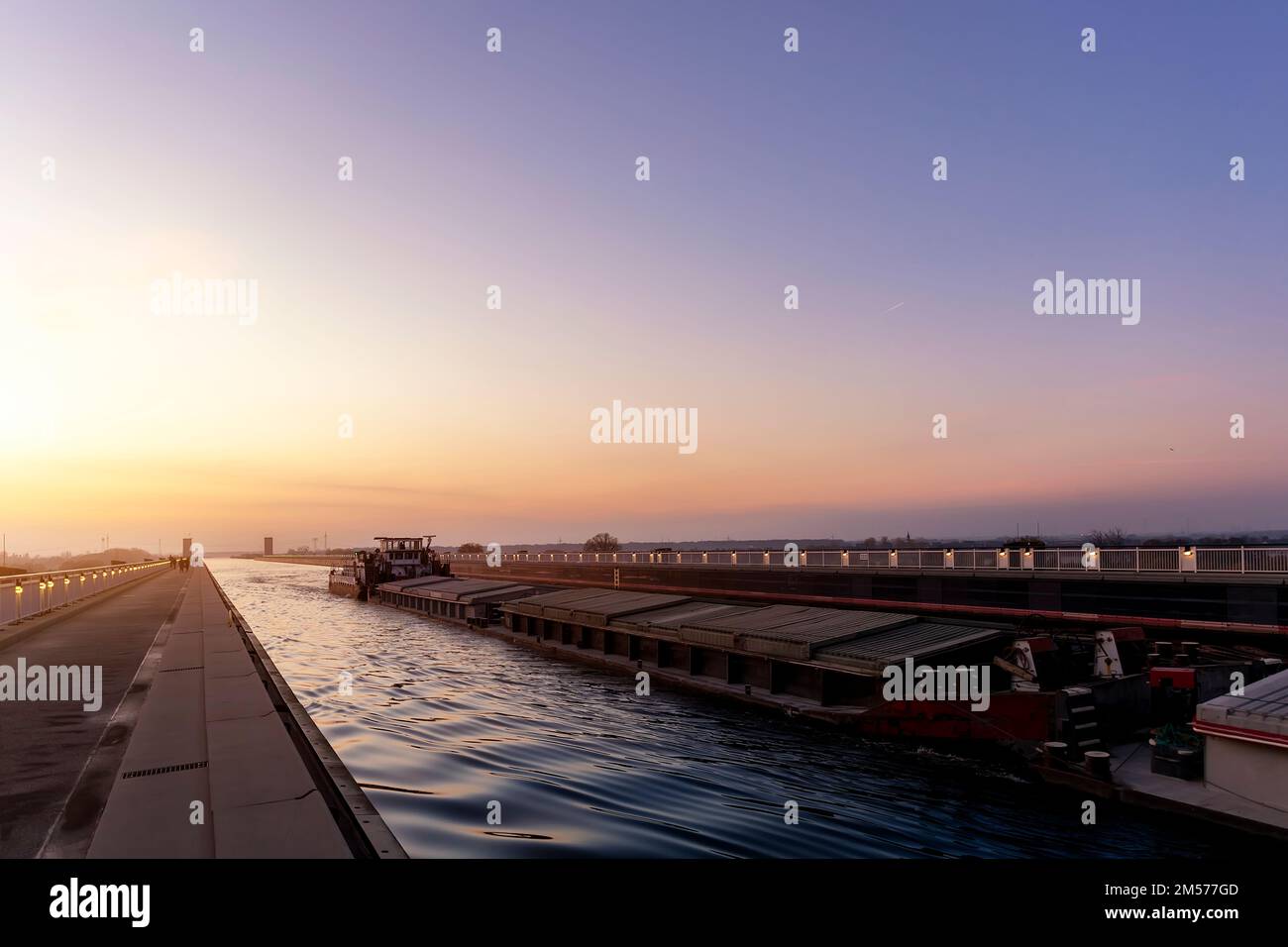 Vista panoramica del grande carico merci tugboat chiatta nave barca vela dal canale interno tedesco Magdeburg ponte contro caldo tramonto cielo backrgound. Acqua Foto Stock