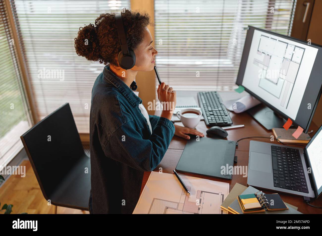 Afro american donna interior designer in cuffie lavora in casa ufficio disegno su tablet grafico Foto Stock