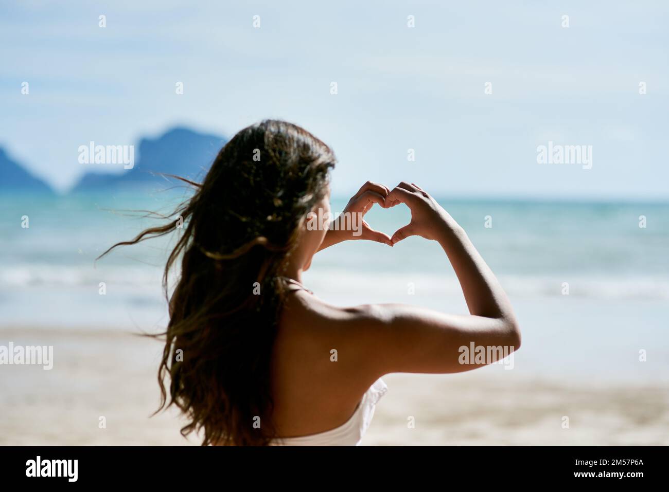 Adoro solo le giornate in spiaggia. una giovane donna che forma un cuore mentre guarda il paesaggio della spiaggia. Foto Stock