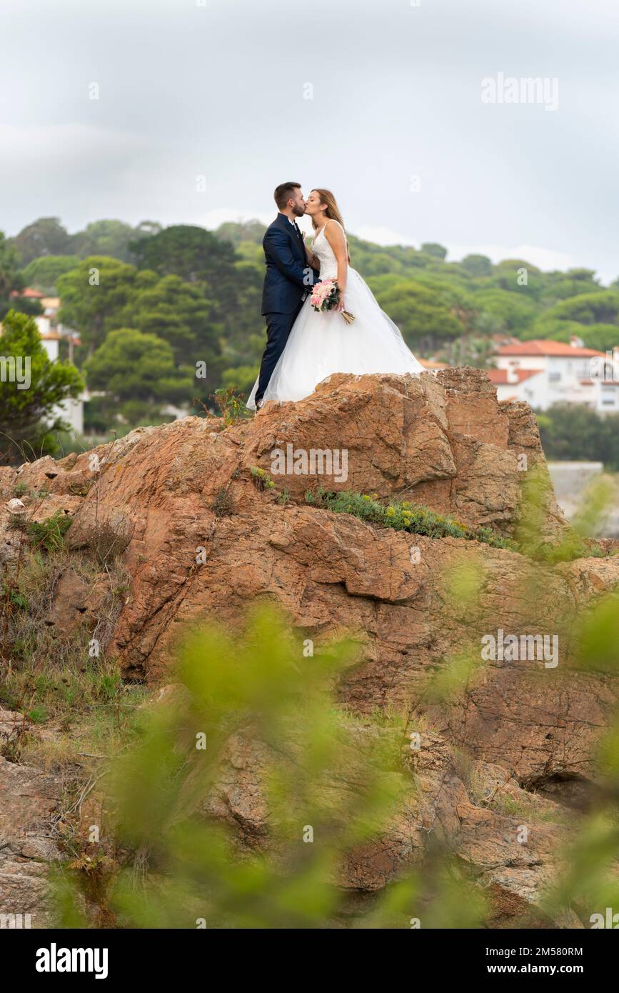 Coppia appena sposata baciandosi e abbracciandosi su alcune rocce vicino alla costa Foto Stock