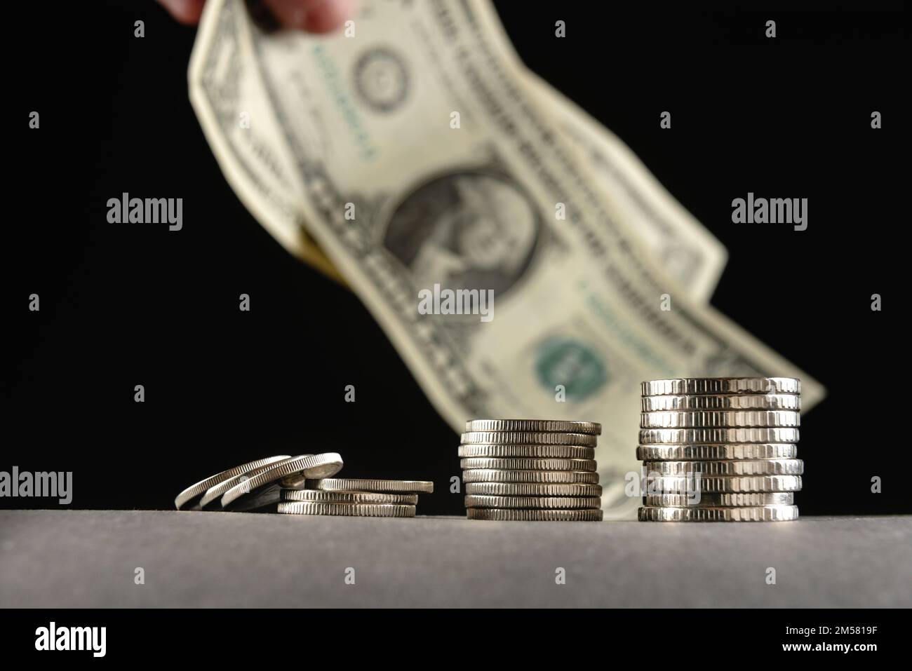 Mucchi di monete in una pila di tagli diversi su sfondo nero e una fattura di vendita degli Stati Uniti sullo sfondo. Investimenti e risparmi. Povertà Foto Stock