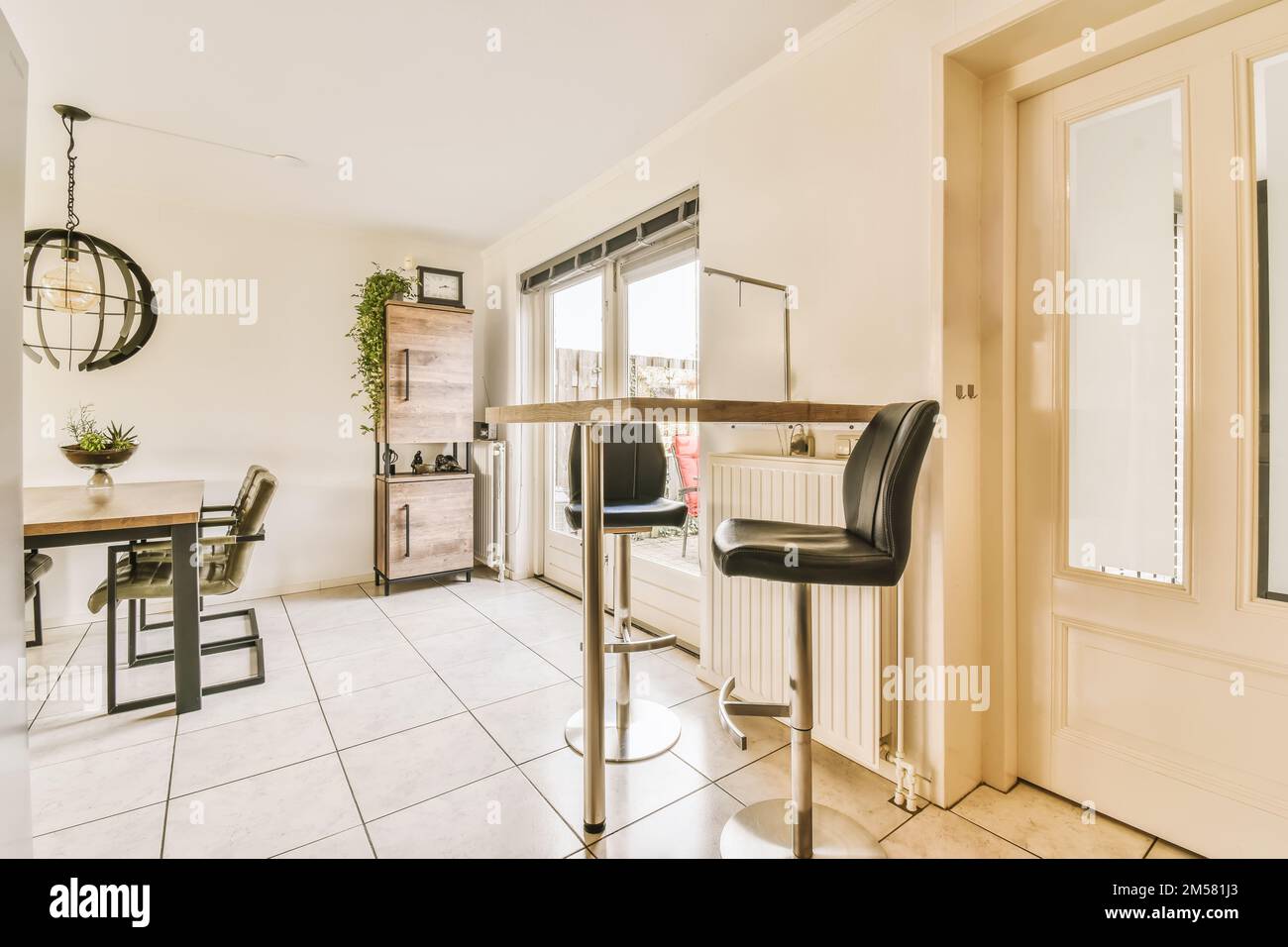 una cucina e zona pranzo in una casa con pavimento in piastrelle bianche, pareti beige e porte si aprono all'esterno Foto Stock