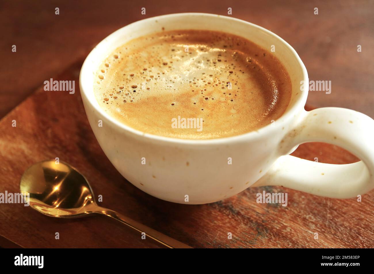 Closeup di un caffè caldo schiumoso con cucchiaino da tè di ottone su tavolo di legno Foto Stock