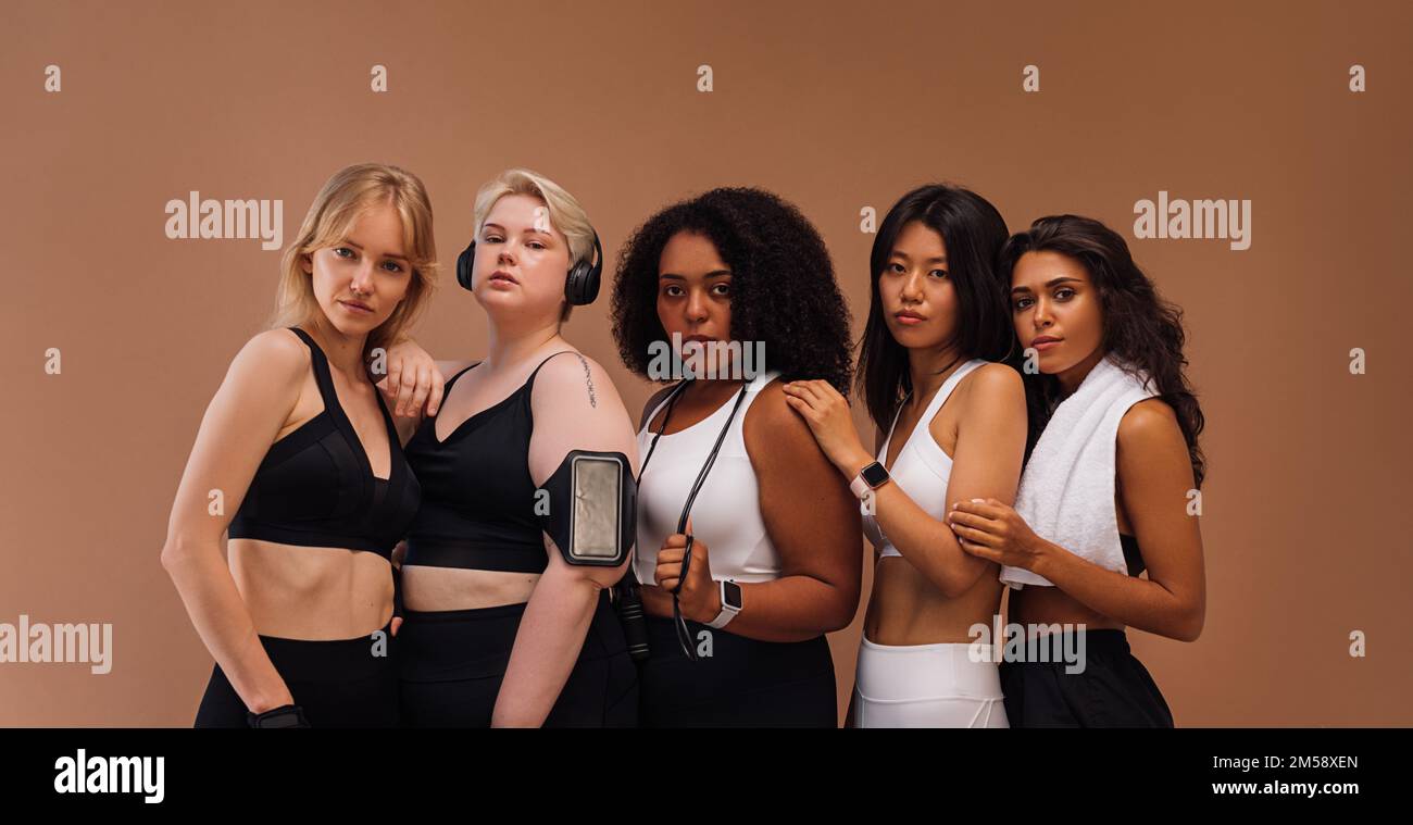Cinque donne in abbigliamento sportivo con diversi tipi di corpo su sfondo marrone Foto Stock