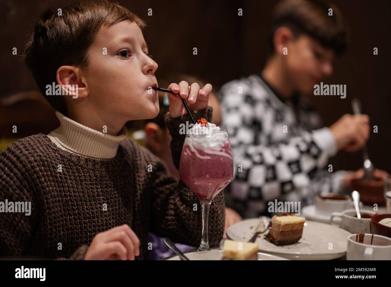 I bambini mangiano dessert insieme nell'accogliente caffetteria e si divertono. Ragazzo bere milkshake. Foto Stock