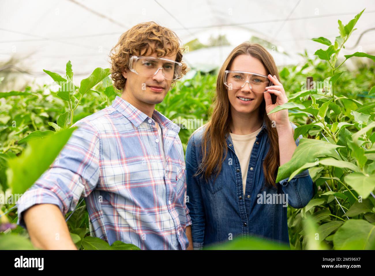 Agronomi in occhiali protettivi che prendono un selfie in una serra Foto Stock