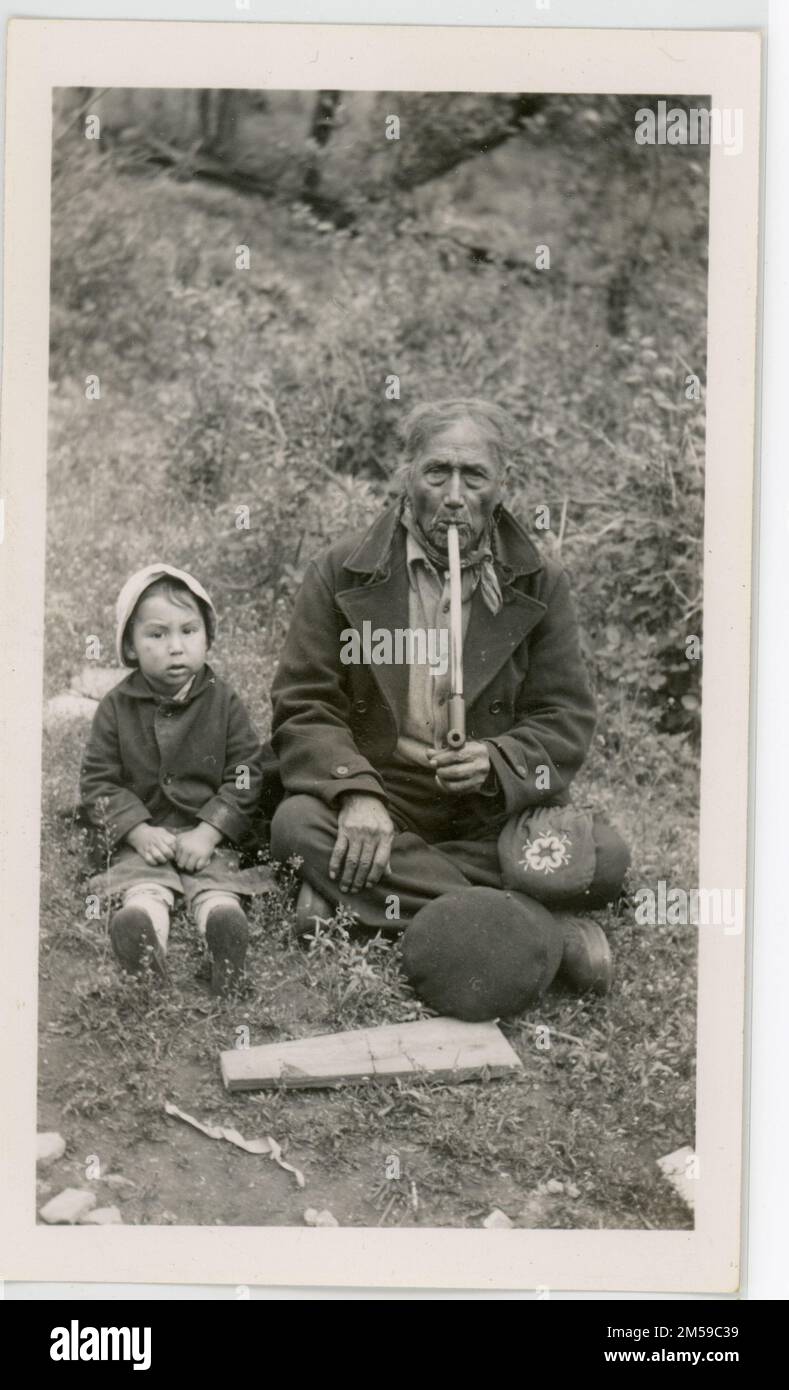 John Bear Smoking Pipe / Bambino accanto. Quest'uomo anziano siede a terra, con un bambino accanto a lui. 1937-01-01T00:00:00. Regione delle pianure centrali (Kansas City, Missouri). Stampa fotografica. Dipartimento dell'interno. Ufficio degli affari indiani. Agenzia Siseton. 9/17/1947-. Fotografie Foto Stock