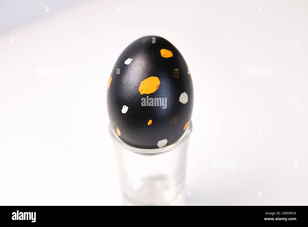 Sfocate un uovo nero con puntini arancioni e bianchi. Primo piano uovo di Pasqua su sfondo bianco. Concetto minimo di celebrazione pasquale. Concetto di armonia dell'equilibrio Foto Stock