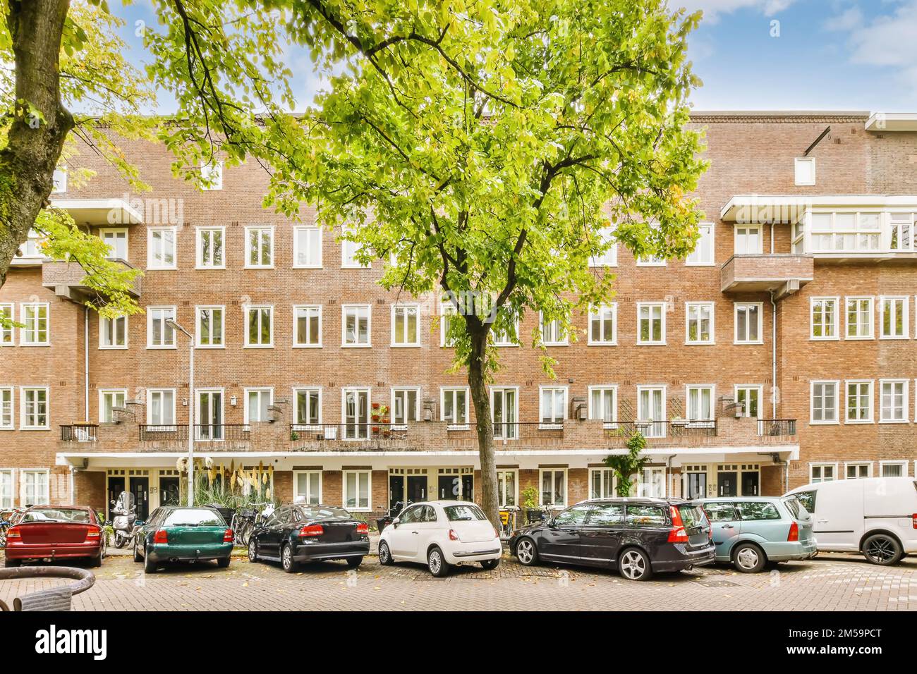 alcune auto parcheggiate di fronte a un grande edificio in mattoni con molte finestre e balle all'ultimo piano sotto Foto Stock