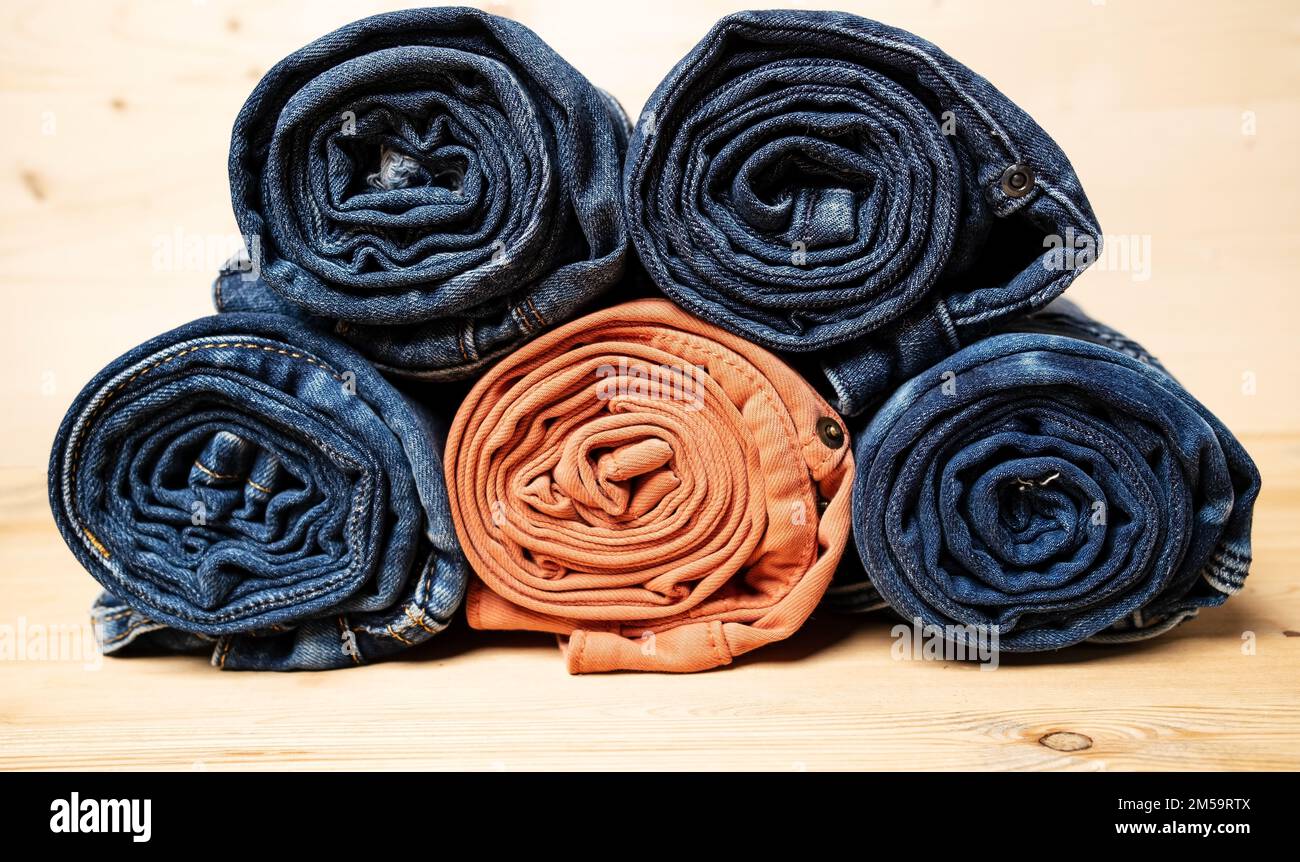 I jeans sono arrotolati e impilati, su uno sfondo di legno. Foto Stock