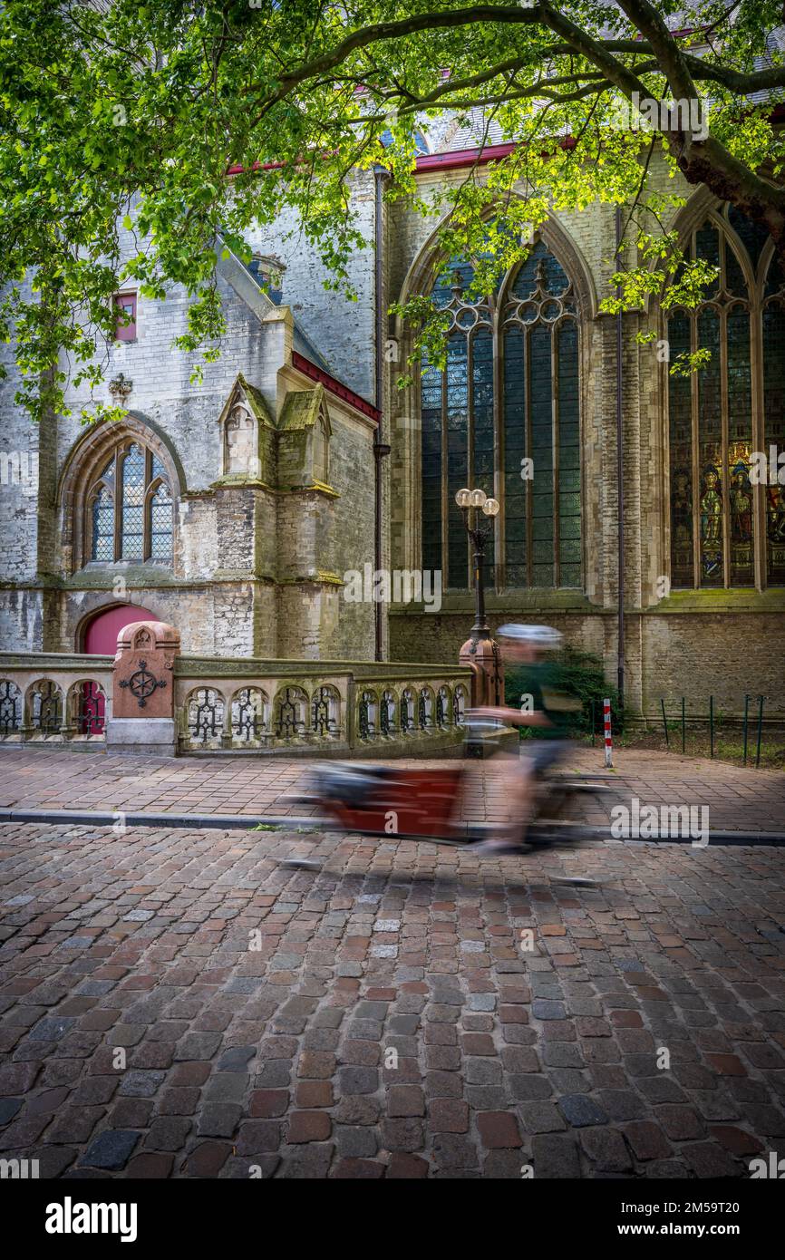 Un movimento verticale offuscato di un uomo in bicicletta su una strada vecchia con un vecchio edificio sullo sfondo a Gand, Belgio Foto Stock