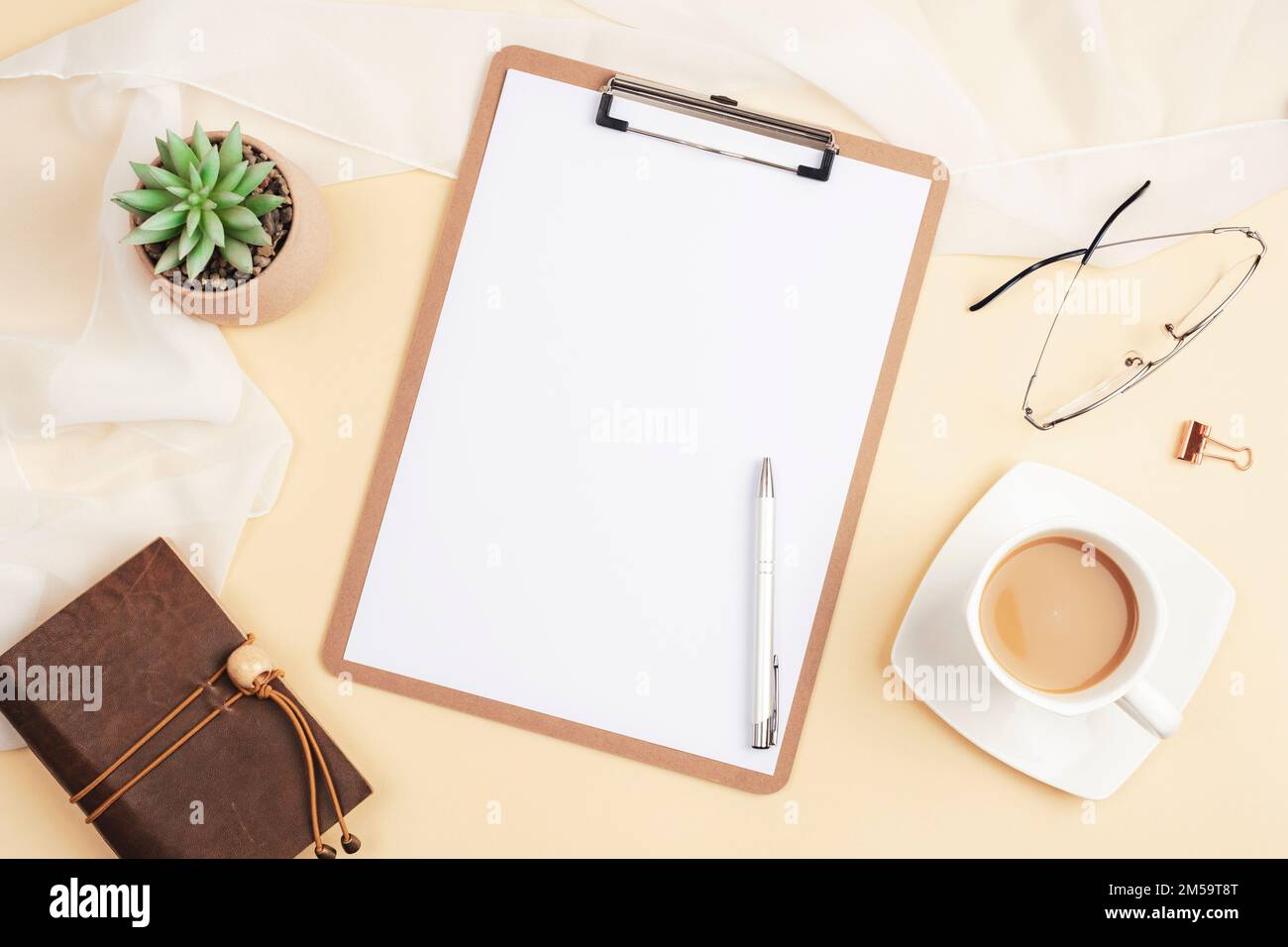 Desktop con appunti vuoti, blocco note, tazza da caffè, piante succulente e accessori su sfondo beige chiaro. Vista dall'alto, piatto, mockup. Foto Stock