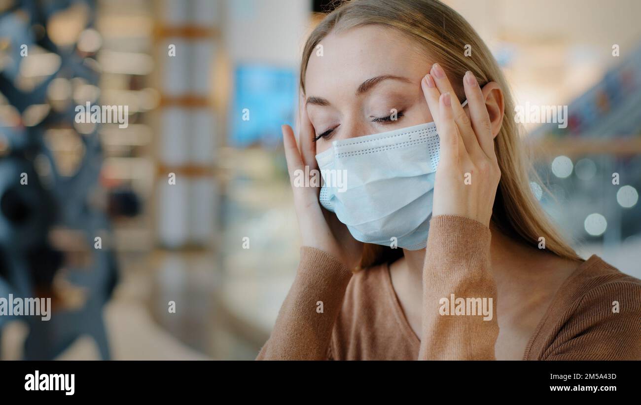 Donna caucasica malato sofferenza bionda ragazza malato donna indossare maschera medica tenere templi fronte sensazione paura influenza sintomi virus coronavirus pandemia Foto Stock