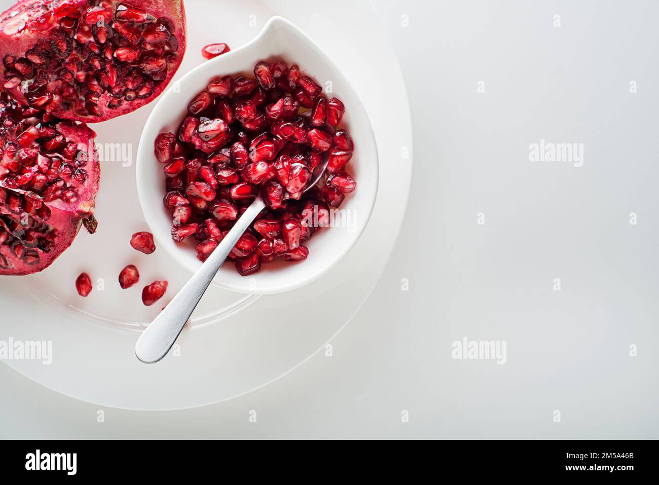 Frutti di melograno sani e maturi, aperti e spelati con semi su piatto bianco Foto Stock