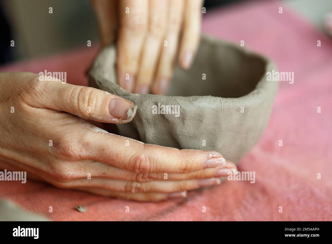 Le mani delle donne impastano l'argilla e scolpiscono una tazza da essa. Il processo di fabbricazione di un prodotto ceramico,primo piano. Foto Stock