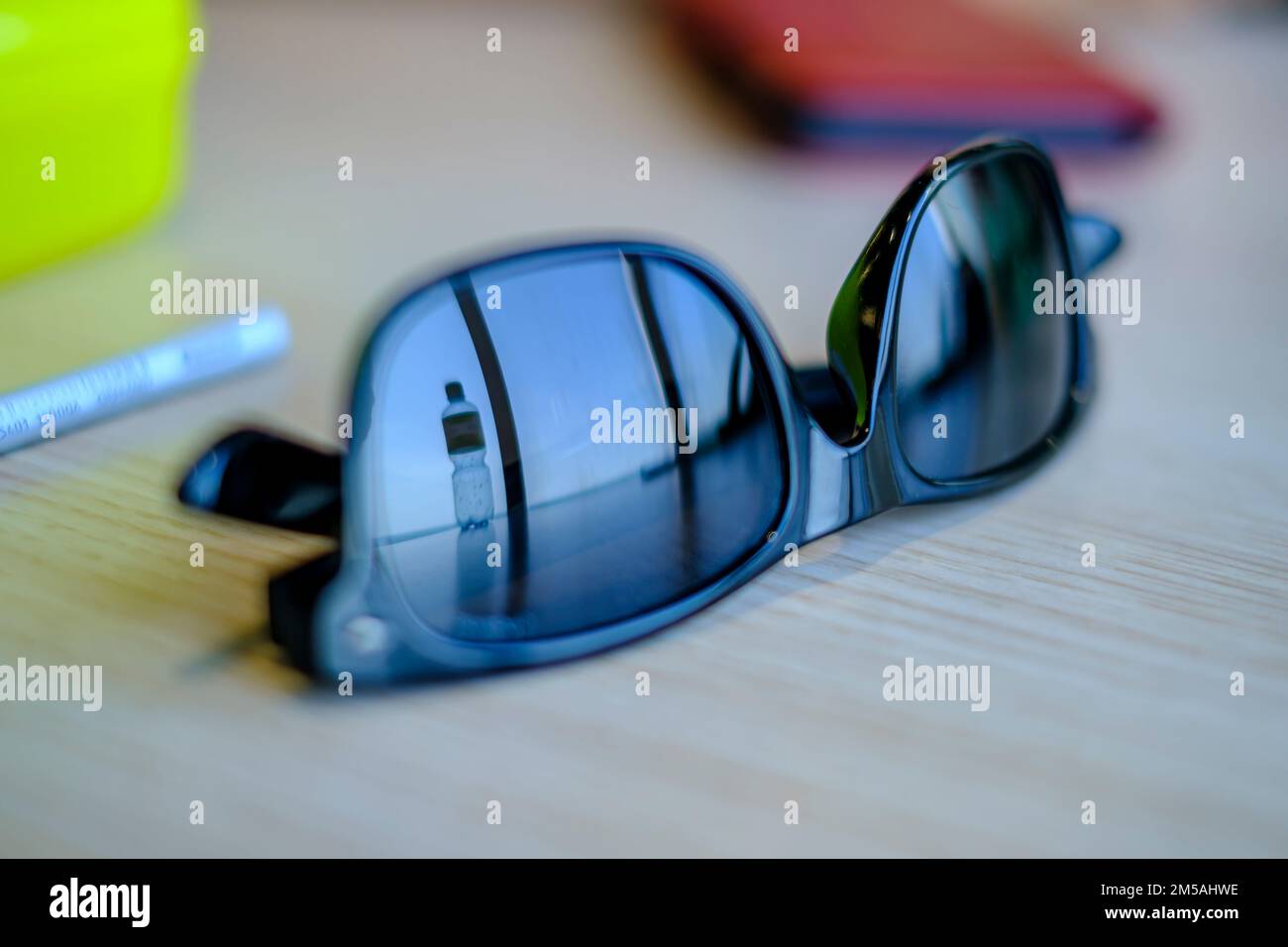 Riflessione di una bottiglia d'acqua nella lente di un occhiali da sole su un tavolo. Foto Stock