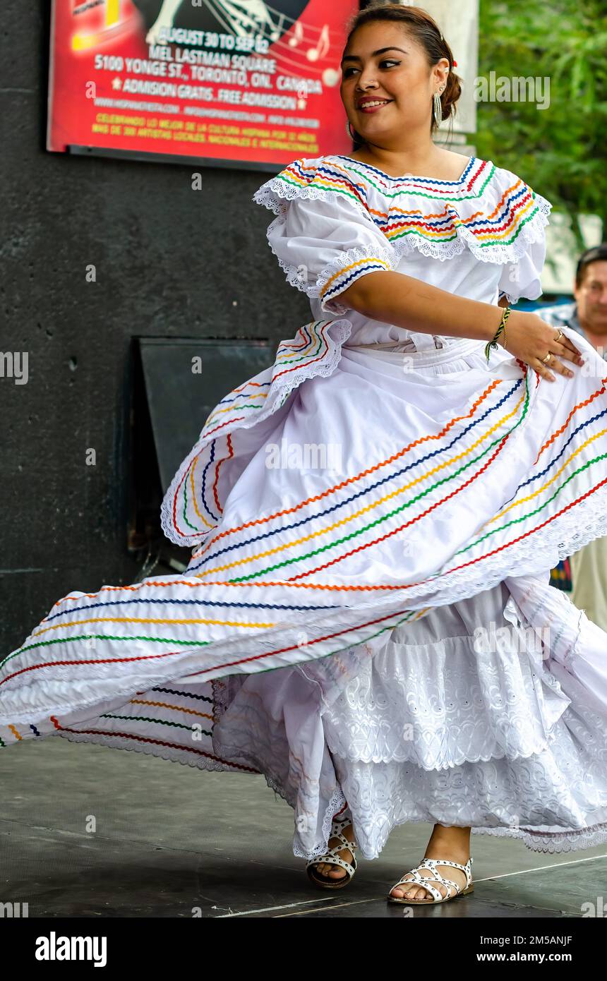 Una donna sorridente indossa abiti tradizionali latinoamericani mentre balla sul palco. L'evento annuale si svolge in piazza Mel Lastman. Foto Stock