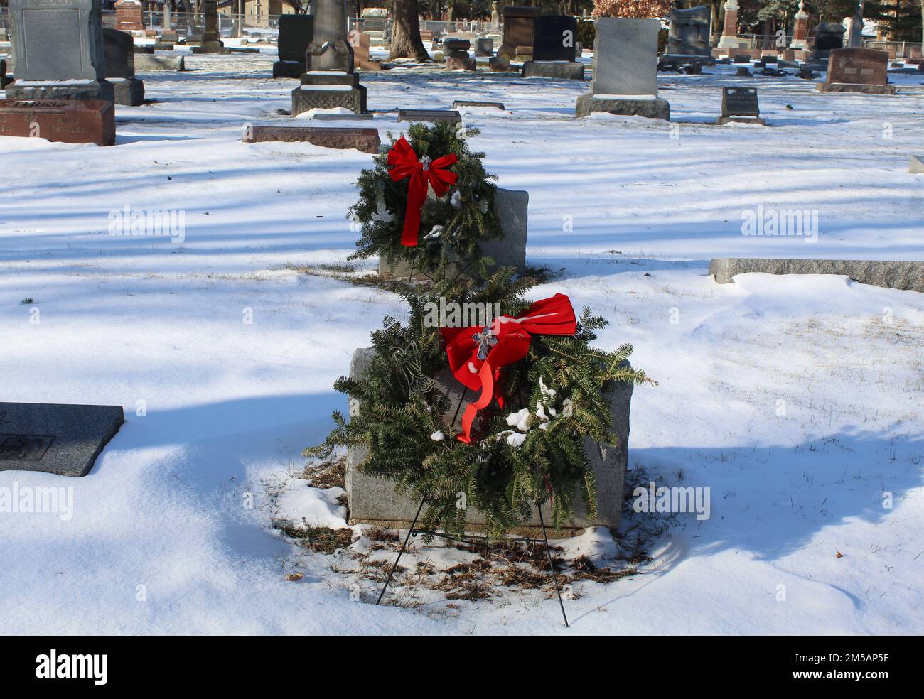Due corone natalizie dietro una lapide in un cimitero suburbano di Chicago con la neve Foto Stock