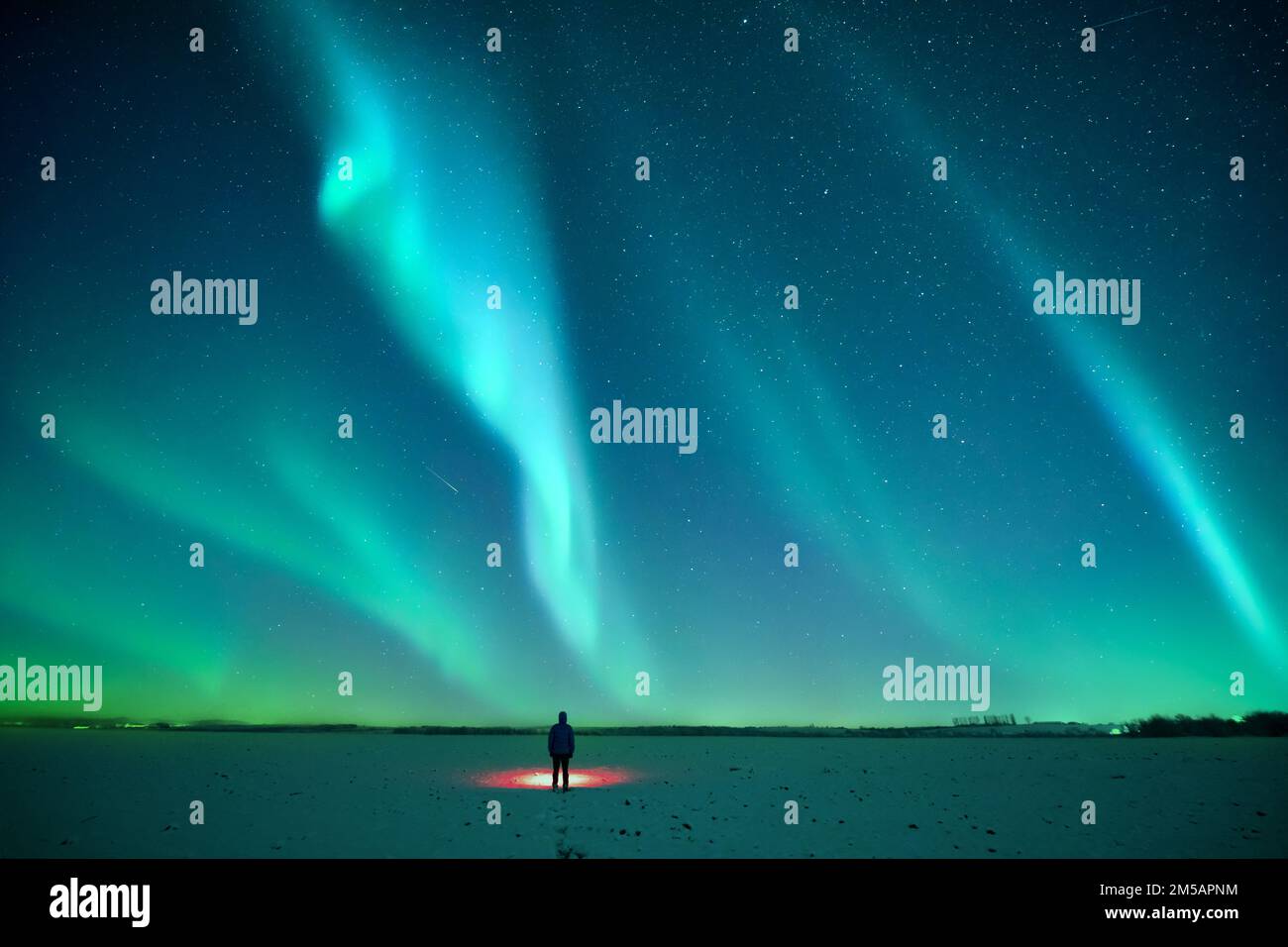 Tourist con torcia rossa su campo innevato sullo sfondo di incredibile cielo stellato con Aurora borealis. Incredibile paesaggio notturno. Luce settentrionale Foto Stock