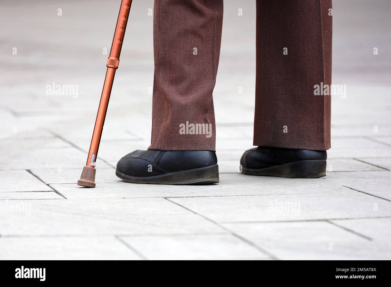 Uomo con bastone da passeggio su una strada, gambe maschili in pantaloni sul marciapiede. Concetto di invalidità, persona che limping Foto Stock