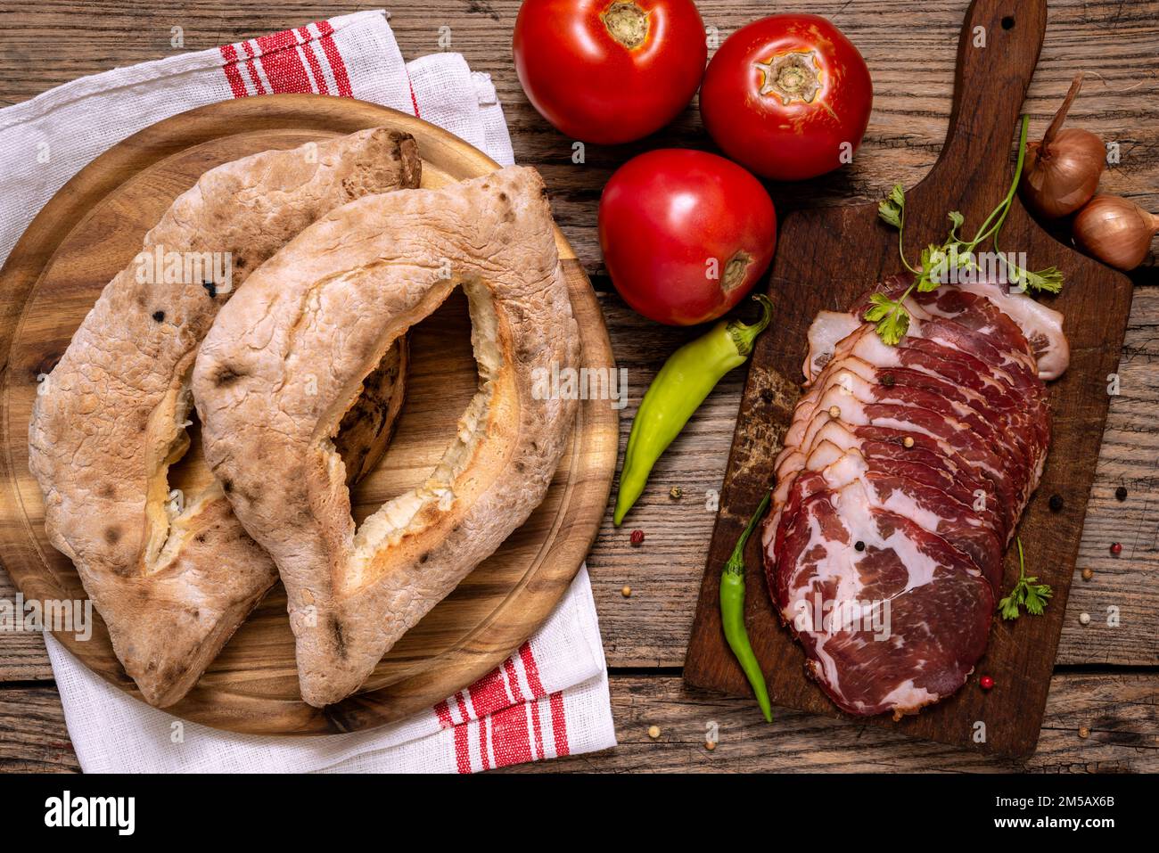 Tradizionale serbo focaccine al forno fatte in casa (lepinja), verdure e tagliere con prosciutto affettato su tavola di legno. Foto Stock