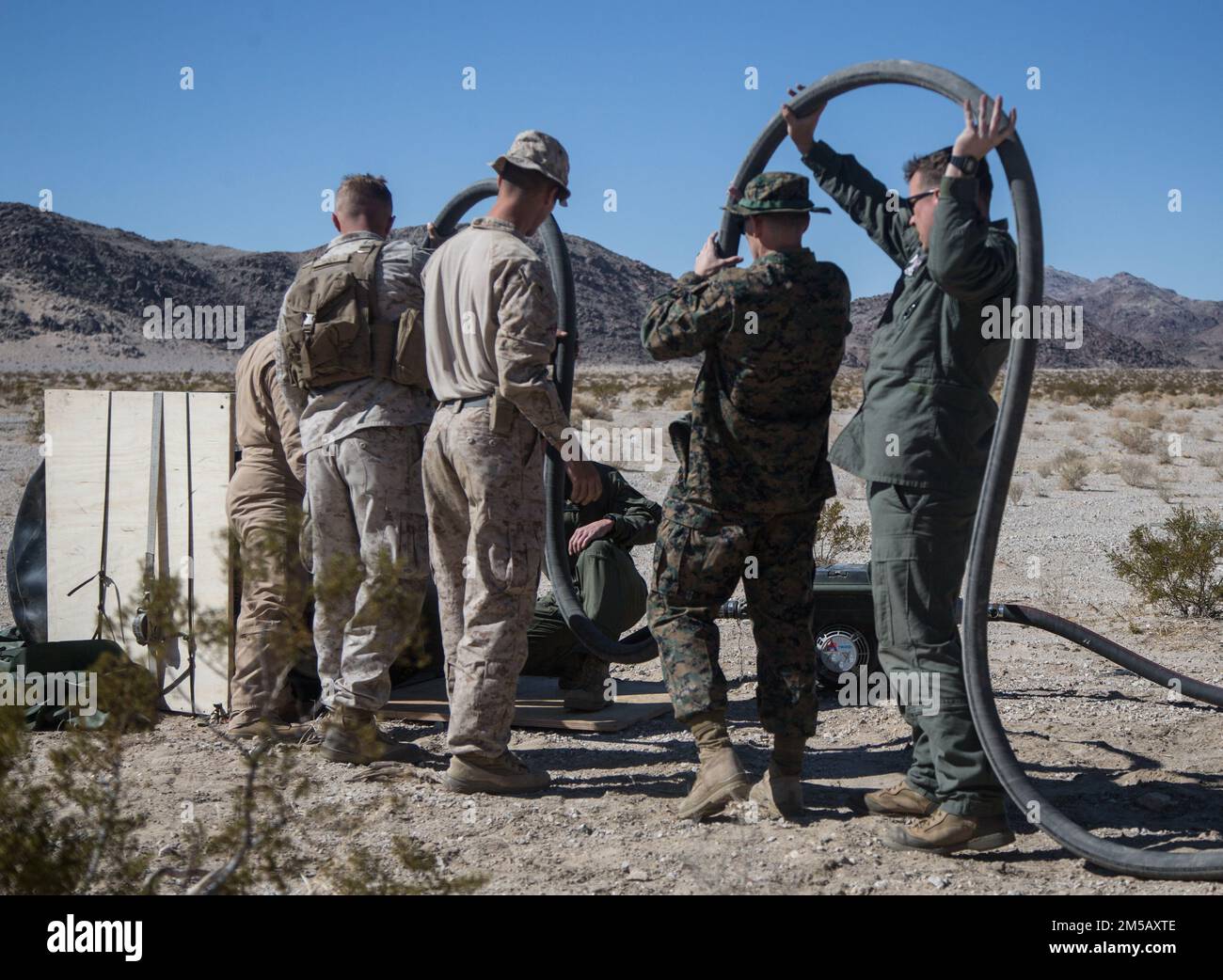 Marines con Marine Wing Support Squadron 372, Marine Aircraft Group (MAG) 39, 3rd Marine Aircraft Wing (MAW) e Marine Light Attack Helicopter Squadron 169, MAG 39, 3rd MAW, Svuotare il tubo del carburante nella camera d'aria che è atterrata nel sistema JPADS (Joint Precision Aerial Delivery System) presso il Marine Corps Air Ground Combat Center Twentynine Palms, California, 16 febbraio 2022. Questo carico del JPADS ha fornito carburante per stabilire un punto di rifornimento di armamento anteriore all'atterraggio per mostrare l'aeromobile come self-serving in ambienti austeri durante la Furia di Inverno 22. Winter Fury 22 sottolinea l'aumento del flusso di informazioni e. Foto Stock