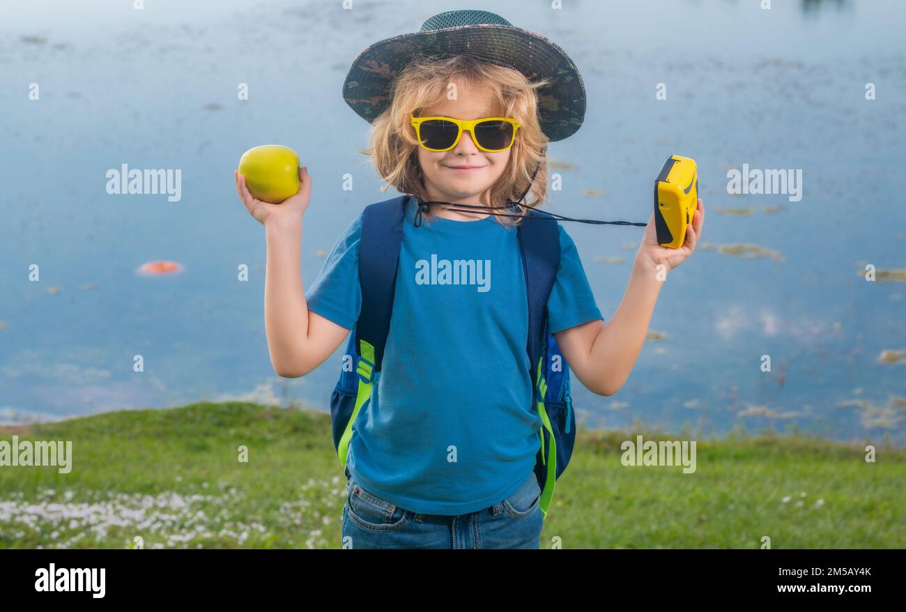 Carino bambino biondo con macchina fotografica indossando cappello explorer e zaino sulla natura. Escursione e avventura in esplorazione per bambini. Foto Stock