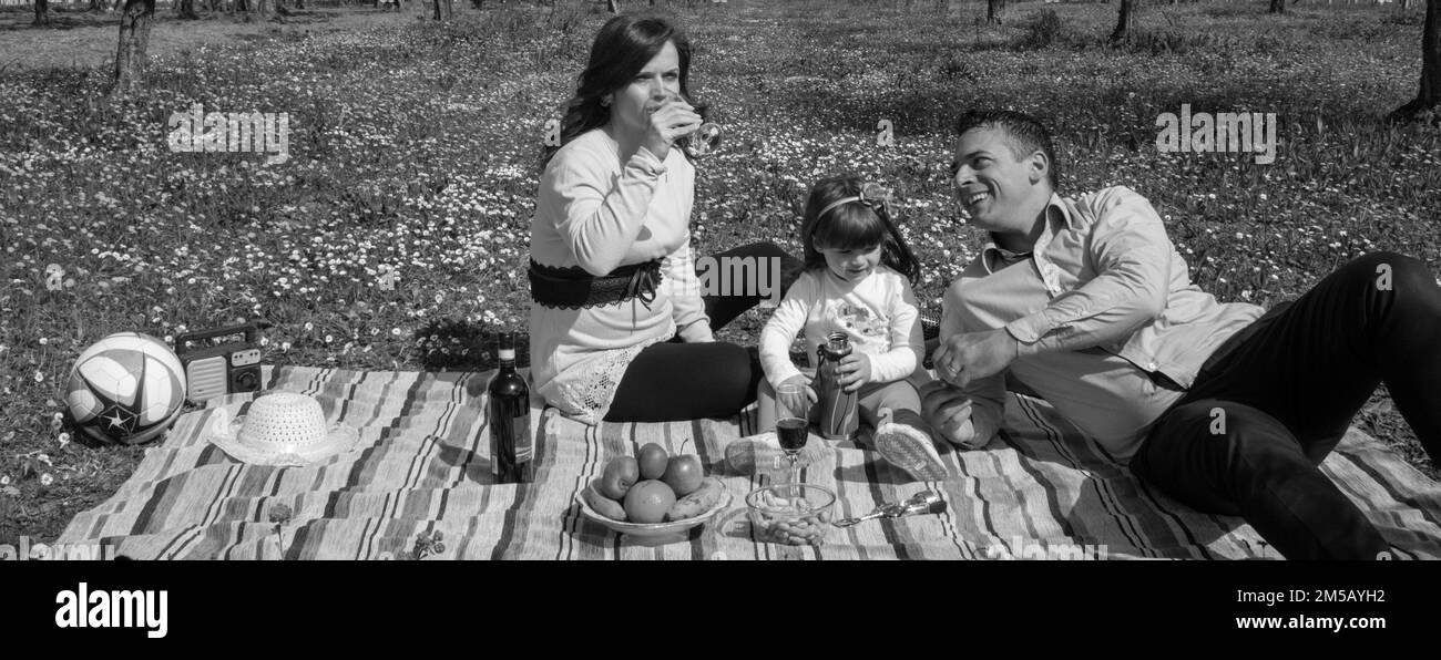Immagine di una famiglia sorridente seduta in un campo fiorito con un picnic. Vacanze in Toscana in famiglia e relax in campagna. Foto Stock