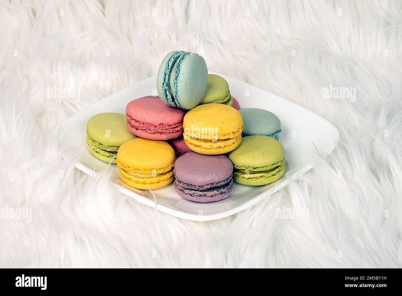 Macaron francesi colorati su un piatto quadrato bianco e pelliccia Foto Stock