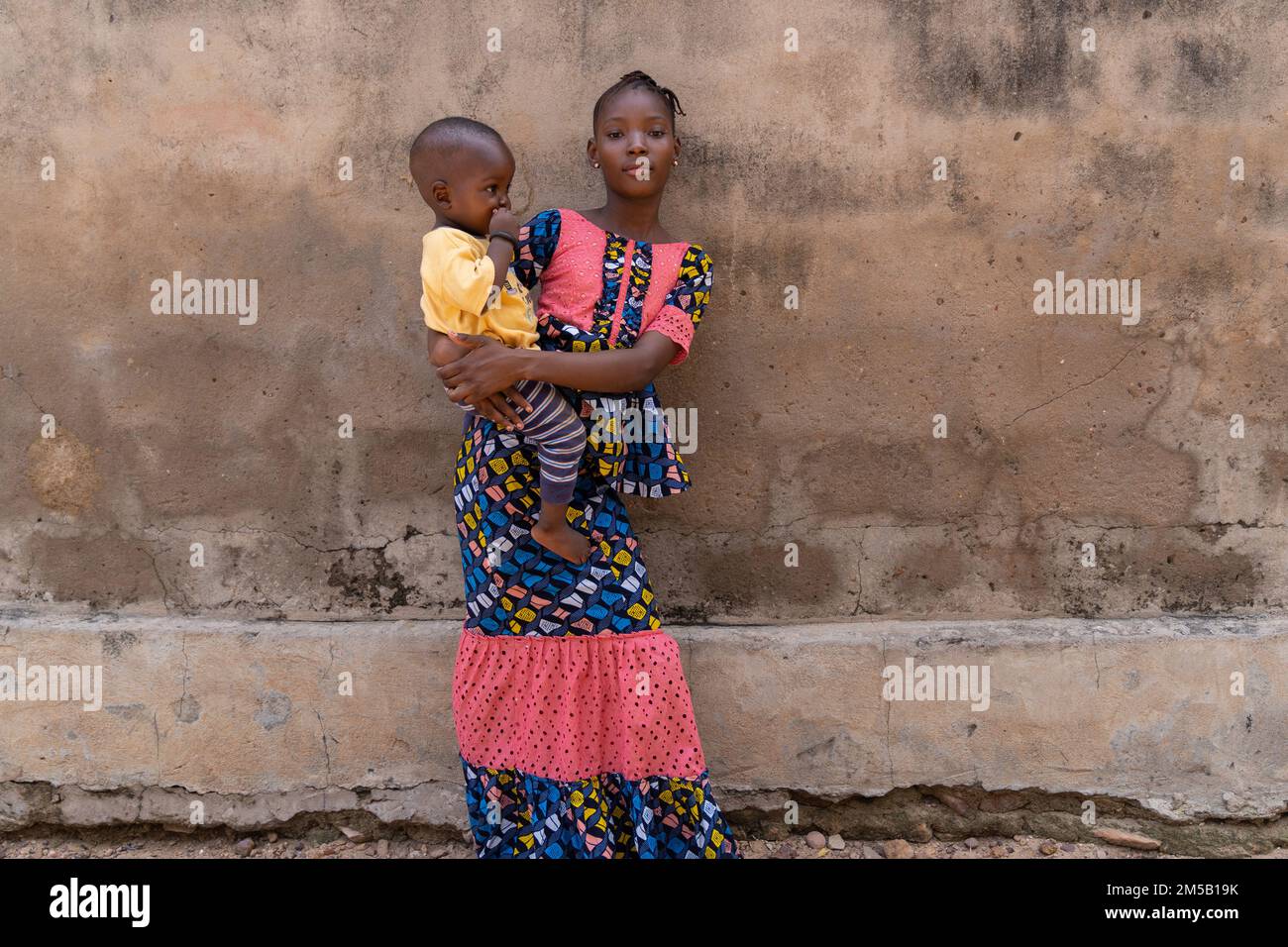 Una giovane ragazza africana fiduciosa che si prende cura di suo piccolo fratello; concetto di disuguaglianza di genere Foto Stock
