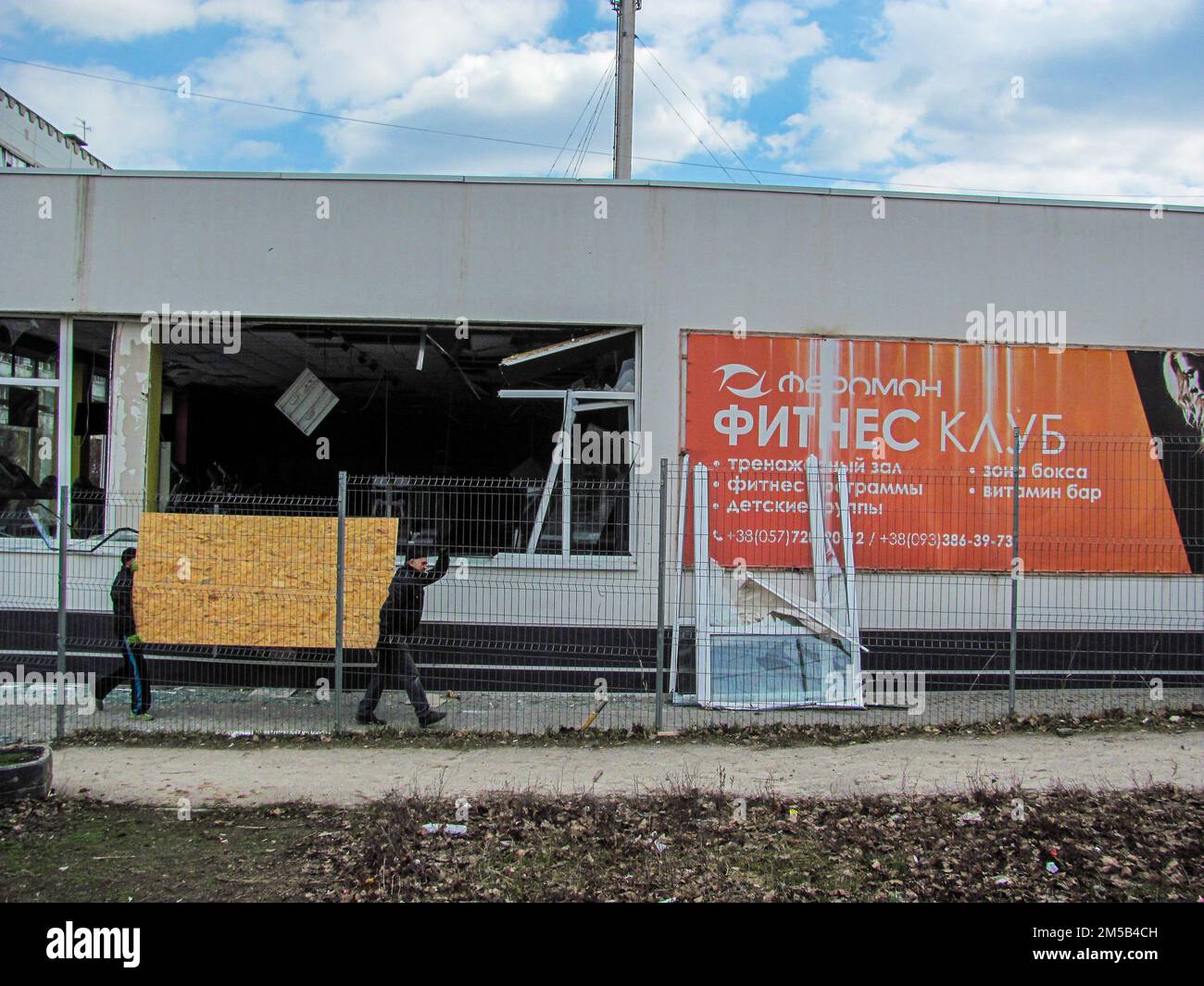 Kharkiv, Ucraina - 05.28.2022: Distrutto bruciato palestra fitness in Kharkov Ucraina rotto vetro ucraino uomini portare compensato porta frammento di costruzione dopo Foto Stock