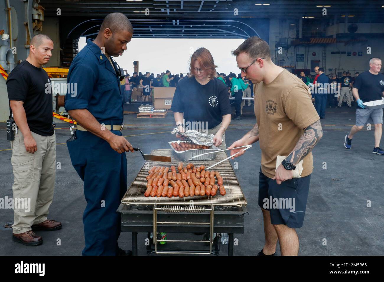 MARE DELLE FILIPPINE (18 febbraio 2022) i marinai grigliano hot dog durante un picnic sulla spiaggia d'acciaio nella baia dell'hangar a bordo della portaerei di classe Nimitz USS Abraham Lincoln (CVN 72). Abraham Lincoln Strike Group è in fase di implementazione pianificata nell'area delle operazioni della flotta 7th degli Stati Uniti per migliorare l'interoperabilità attraverso alleanze e partnership e al tempo stesso fungere da forza di risposta pronta a sostegno di una regione indomPacifico libera e aperta. Foto Stock