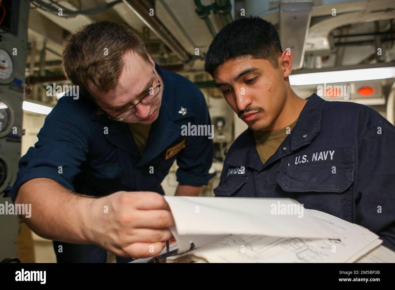 PHILIPPINE SEA (24 febbraio 2022) Kyle Dermody, compagno di Electrician 2nd Class, di sinistra, da Portland, Conn., e il Fireman di Electrician Mate Mario Hernandez, di Seminole, Texas, rivedere un manuale tecnico per trovare fili in corto circuito a bordo della portaerei di classe Nimitz USS Abraham Lincoln (CVN 72). Abraham Lincoln Strike Group è in fase di implementazione pianificata nell'area delle operazioni della flotta 7th degli Stati Uniti per migliorare l'interoperabilità attraverso alleanze e partnership e al tempo stesso fungere da forza di risposta pronta a sostegno di una regione indomPacifico libera e aperta. Foto Stock