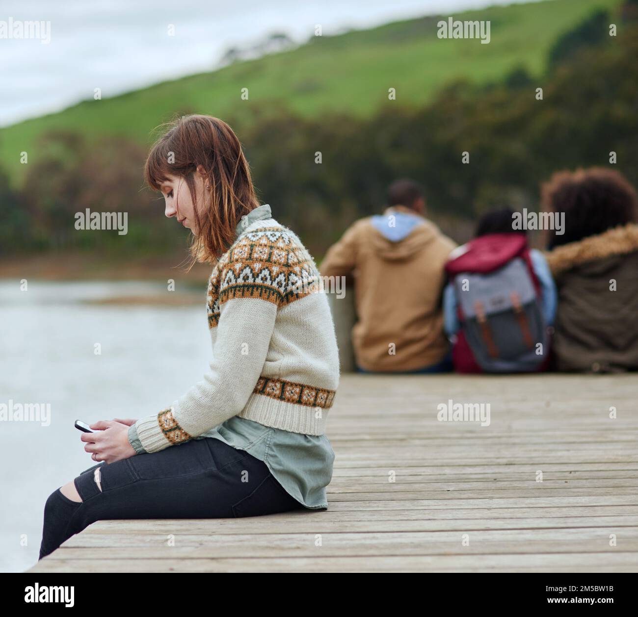 Godendosi un momento a se stessa. una giovane donna che invia un sms mentre si siede sul molo vicino a un lago. Foto Stock