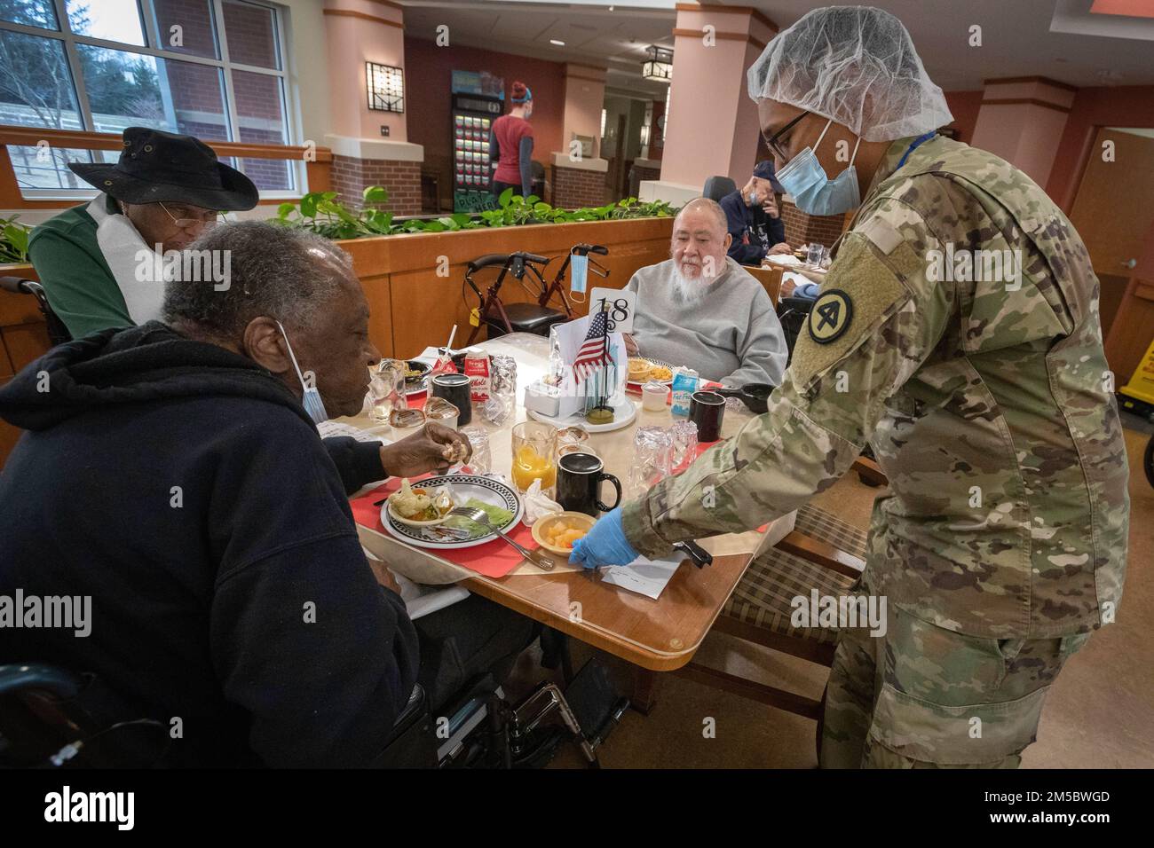 STATI UNITI Rayas Ali, Charlie Company, 104th Brigade Engineer Battalion, 44th Fanteria Brigade Combat Team, New Jersey Army National Guard, Hands James Dow, residente nella New Jersey Veterans Memorial Home di Vineland, il suo deserto nella sala da pranzo di The Home a Vineland, New Jersey, 24 febbraio 2022. Nella foto si trovano anche Alphonso Smith, a sinistra, e Leroy Pierce, secondo da destra. Ali sta servendo i residenti della Casa nel Food Services Department. Più di 70 soldati della Guardia Nazionale del New Jersey e gli Airmen stanno servendo come assistenti infermieristici certificati e nei servizi alimentari, contagio Foto Stock